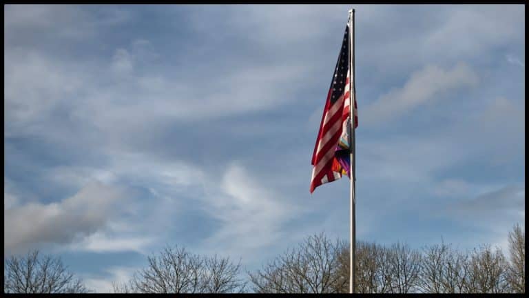 US flag on a flagpole with a progress pride flag beneath it.