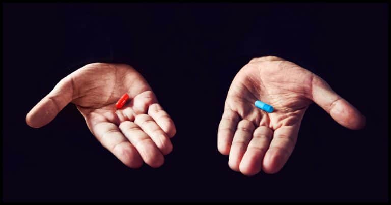 A hand holding a red pill, and a hand holding a blue pill.